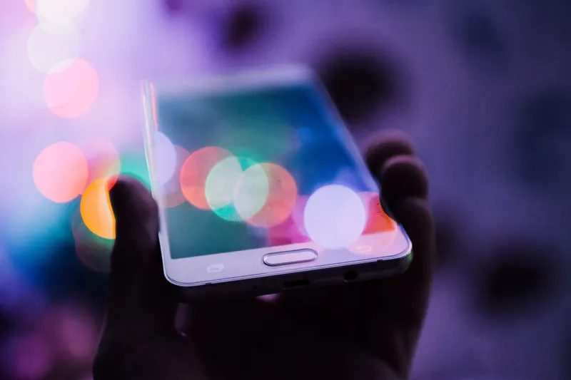 Mano che regge uno smartphone tra luci colorate